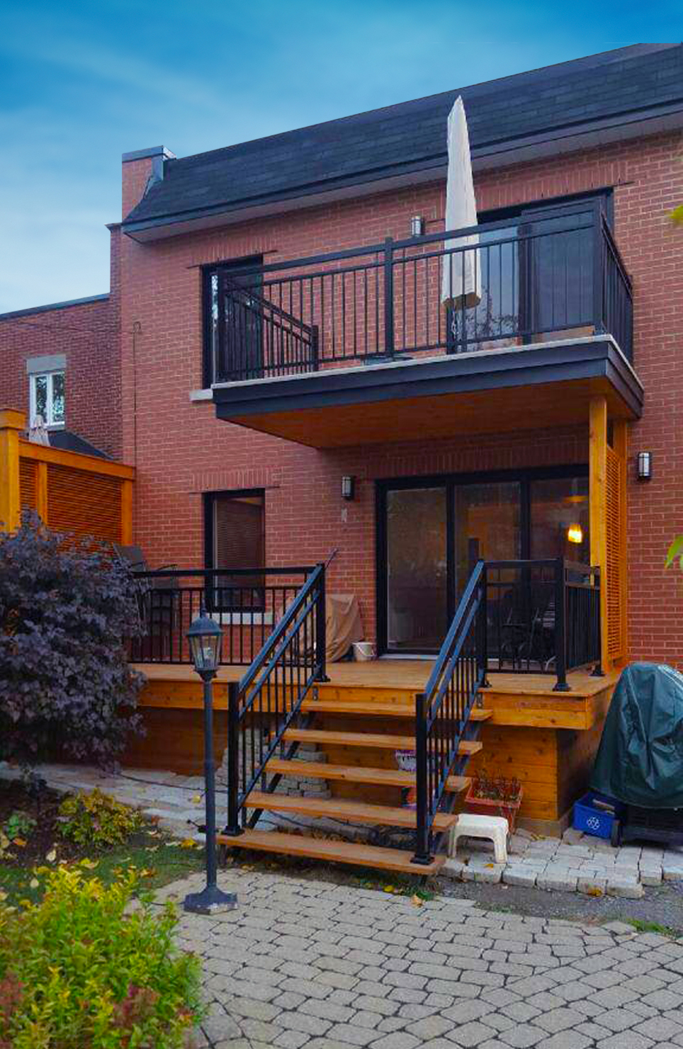 Maison en briques avec balcon en fibre de verre à l’étage, offrant une terrasse extérieure durable au-dessus du patio en bois.