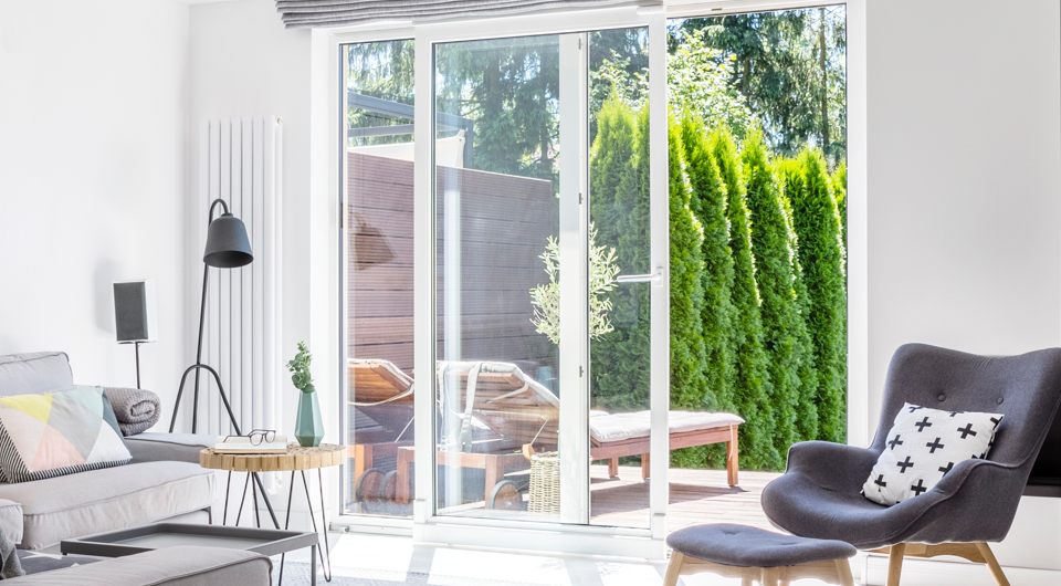 Salon moderne avec vue sur la terrasse extérieure à travers une porte patio coulissante en verre, offrant une transition fluide entre l’intérieur et l’extérieur.