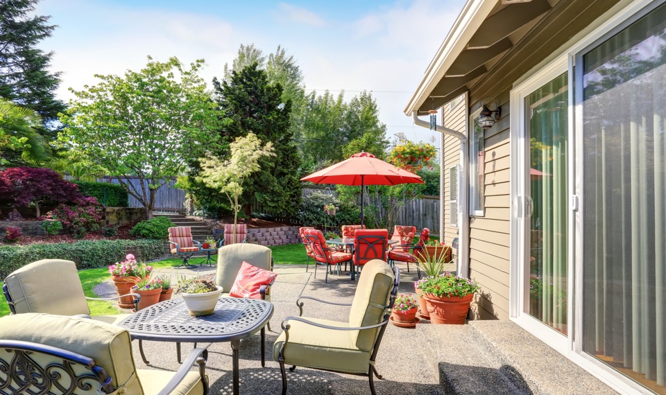 Terrasse extérieure avec mobilier de jardin, accessible par une porte patio coulissante, offrant une vue sur un espace vert aménagé et ensoleillé.